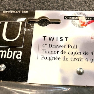 May include: A black and white packaging label for a 4 inch chrome drawer pull from Umbra. The label features the Umbra logo and the text "TWIST 4" Drawer Pull Tirador de cajón de 4" Poignée de tiroir 4 po".