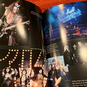 Puede incluir: Una revista con fotos de conciertos de las bandas de rock KISS y Judas Priest. La foto de KISS muestra a un miembro de la banda tocando el bajo. La foto de Judas Priest muestra a la banda actuando en el escenario. La revista est&aacute; abierta sobre una superficie naranja.