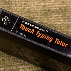 May include: Black TI-99/4A Command Module cartridge with a white label that reads "Touch Typing Tutor" and "Command Module TM" with a copyright symbol and "1982 TI".