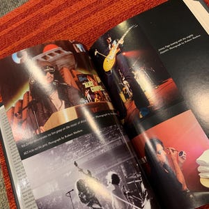 Puede incluir: Libro abierto con fotograf&iacute;as de conciertos de Rob Zombie, Jimmy Page y Alice Cooper. El libro est&aacute; sobre una superficie con estampado rojo y gris. El texto incluye "MCS kicks out the jams" y cr&eacute;ditos del fot&oacute;grafo.
