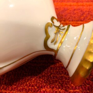 K&ouml;nnte beinhalten: Nahaufnahme eines wei&szlig;en Keramikobjekts mit goldenen Akzenten. Das Objekt hat eine geschwungene Form mit breitem Sockel und einem dekorativen Golddesign. Die goldene Verzierung verleiht dem St&uuml;ck einen Hauch von Eleganz.