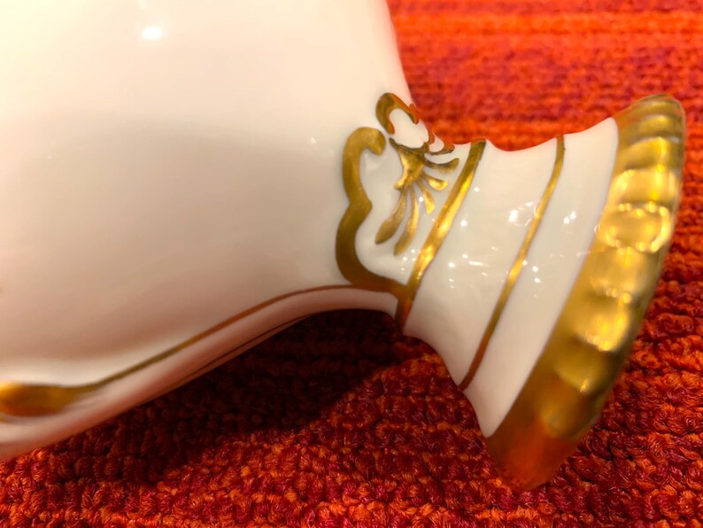 K&ouml;nnte beinhalten: Nahaufnahme eines wei&szlig;en Keramikobjekts mit goldenen Akzenten. Das Objekt hat eine geschwungene Form mit breitem Sockel und einem dekorativen Golddesign. Die goldene Verzierung verleiht dem St&uuml;ck einen Hauch von Eleganz.