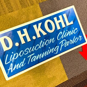 Letrero de hojalata pintado a mano vintage con el lema "Kohl Liposuction Clinic and Tanning Parlor" (Clínica de liposucción y salón de bronceado Kohl) Letrero de metal publicitario retro