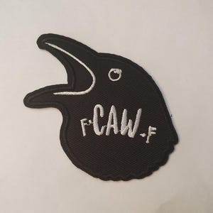 May include: Black embroidered iron-on patch of a crow with its beak open and the text "F*CAW*F" in white.