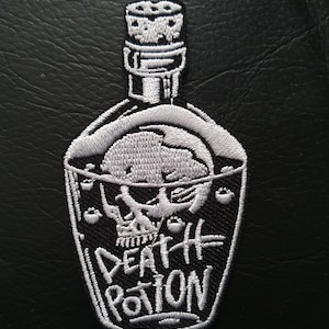 Puede incluir: Parche bordado blanco de una botella de vidrio con una calavera en su interior y el texto "DEATH POTION" sobre un fondo negro.