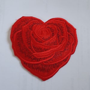 Puede incluir: Rosa roja bordada en forma de corazón. La rosa es un símbolo popular de amor y romance.