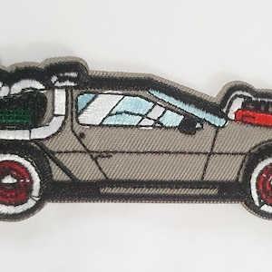 May include: A grey embroidered patch of the DeLorean time machine from the Back to the Future film. The car is facing right and has a red and white tyre on the left side and a red and white tyre on the right side.