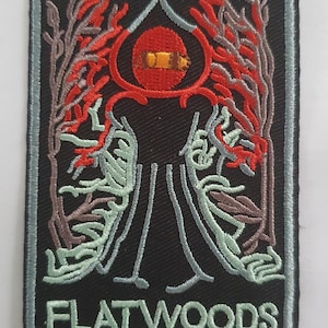 Op de afbeelding: Een zwarte geborduurde patch met de tekst "Cryptozoology Tracking Society" en "Flatwoods Monster" in wit. De patch toont een gestileerde afbeelding van een wezen met een rood oog en een zwart lichaam.