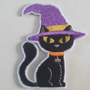 Puede incluir: Parche bordado para planchar de un gato negro con un sombrero de bruja morado con un borde amarillo y un collar naranja. El gato tiene ojos amarillos y un contorno blanco.
