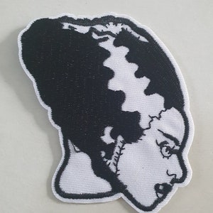 Könnte beinhalten: Schwarz-weiß gestickter Bügel-Patch mit dem Gesicht einer Frau mit Nähten an Hals und Haaren. Die Frau hat einen überraschten Gesichtsausdruck.