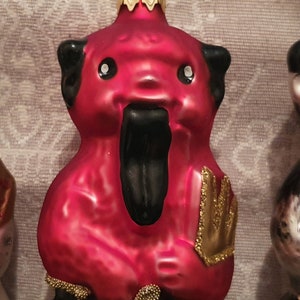 Könnte beinhalten: Roter und schwarzer Weihnachtsschmuck in Bärenform mit langer schwarzer Zunge. Der Bär hat schwarze Ohren und goldfarbene Details. Der Schmuck hat eine goldfarbene Metallkappe und eine Schlaufe zum Aufhängen.