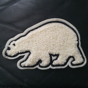 May include: White polar bear patch with black outline, sewn on a black leather surface.