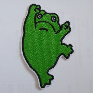 May include: Green embroidered iron-on patch of a frog with its arms raised in the air.