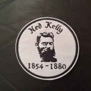 Könnte beinhalten: Weißer gestickter Aufnäher mit einem Schwarzweißbild von Ned Kelly, einem berühmten australischen Outlaw. Der Aufnäher trägt den Text "Ned Kelly" und "1854 - 1880" in Schwarz.