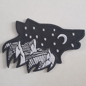 Pode incluir: Patch bordado com a silhueta da cabeça de um lobo com um design de céu noturno. O patch preto tem detalhes bordados brancos de estrelas, uma lua crescente e picos de montanhas estilizados. Adequado para jaquetas, bolsas ou outros itens de tecido.