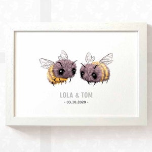 Può includere: Una stampa incorniciata bianca con due api di cartone animato che si guardano. Le api sono pelose e hanno strisce gialle e nere. Il testo sotto le api dice "Lola & Tom * 03.10.2020 *"