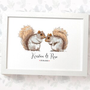 Könnte beinhalten: Gerahmter Druck mit einer Aquarellillustration von zwei Eichhörnchen. Sie sind mit grauem und braunem Fell und flauschigen Schwänzen dargestellt. Die Namen "Kristan & Rose" und das Datum "29.06.2025" sind darunter geschrieben.