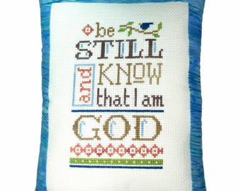 Almohada de punto de cruz terminada con versículo bíblico "Quédate quieto y conoce", completa, para colocar en un estante con fe.