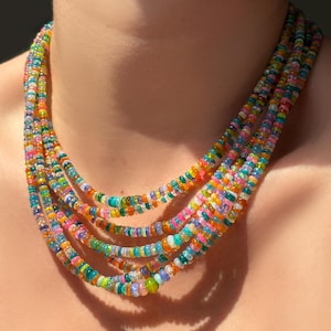 May include: A multi-strand necklace composed of small, colorful beads. The beads are a mix of vibrant colors including pink, orange, green, and blue. The necklace is worn around the neck, with the strands cascading down.