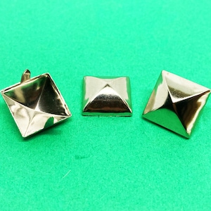 May include: Three silver pyramid-shaped studs with a flat base. The studs are on a green surface.