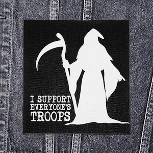 Może przedstawiać: Czarna kwadratowa naszywka z białą sylwetką Grim Reapera trzymającego kosę. Tekst "I SUPPORT EVERYONE'S TROOPS" jest wydrukowany na dole na biało. Naszywka jest pokazana na dżinsowej kurtce.