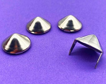 May include: Four silver-colored metal cone-shaped studs with smooth, reflective surfaces. Three of the studs are positioned with their pointed tops facing upward, while one stud is inverted to show the two metal prongs extending from its base.