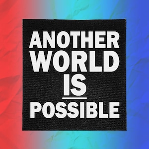 Può includere: Una toppa quadrata in tessuto nero con il testo bianco "ANOTHER WORLD IS POSSIBLE" in un carattere grassetto senza grazie. La scritta è disposta su quattro righe con una linea orizzontale che separa le parole "IS" e "POSSIBLE" al centro.