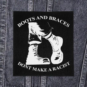 May include: Square black and white patch featuring the text "BOOTS AND BRACES DON'T MAKE A RACIST" and an illustration of legs wearing boots and socks. The patch is set against a denim jacket.