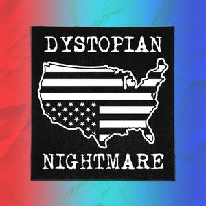 May include: A square black fabric patch featuring a white outline of the United States map filled with a striped and star pattern. The word DYSTOPIAN is printed in white capital letters above the map, and NIGHTMARE is printed below in white.
