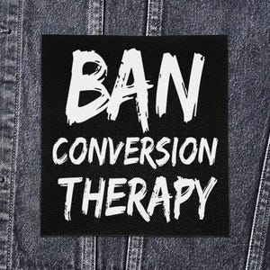 May include: Black square patch with the words "BAN CONVERSION THERAPY" in white, brush-style lettering. The patch is displayed on a denim jacket.