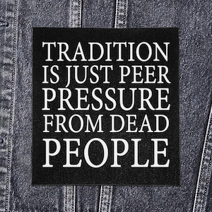 Op de afbeelding: Een zwart vierkant embleem met witte tekst die luidt: "TRADITION IS JUST PEER PRESSURE FROM DEAD PEOPLE." De patch is geplaatst tegen een denim jas achtergrond.