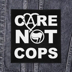 May include: Black square patch with white text and graphics. The text reads "CARE NOT COPS" with a heart-shaped symbol and a flag within a circle. The patch is displayed on a denim jacket.
