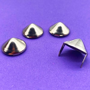 Può includere: Quattro borchie metalliche a forma di piramide argentate, tre con base piatta e una con base quadrata.