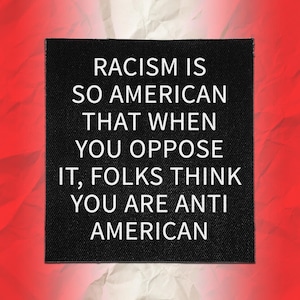 May include: A square black fabric patch featuring white embroidered text which reads: RACISM IS SO AMERICAN THAT WHEN YOU OPPOSE IT, FOLKS THINK YOU ARE ANTI AMERICAN. The patch has a clear woven texture and is placed on a red and white background.