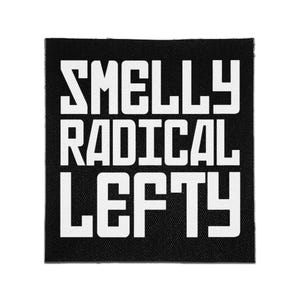 May include: A square black fabric patch featuring the white text "SMELLY RADICAL LEFTY" in a bold, sans-serif, block-style font. The design is centered on the patch, which has a visible woven texture throughout the black background.