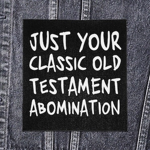 May include: Black square patch with white text that reads "JUST YOUR CLASSIC OLD TESTAMENT ABOMINATION." The patch is set against a denim background.