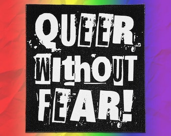May include: A square black fabric patch featuring the white distressed-style text QUEER WITHOUT FEAR! in a bold, blocky font. The lettering has a weathered, textured appearance against the solid black background of the patch material.