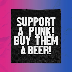 Peut inclure: Un écusson carré en tissu noir avec le texte blanc SUPPORT A PUNK! BUY THEM A BEER! écrit dans une police grasse sans empattement. L'écusson présente une texture tissée visible et des bords nets, offrant un contraste élevé sur fond sombre.
