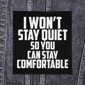 May include: Black square patch with white text: "I WON'T STAY QUIET SO YOU CAN STAY COMFORTABLE." The patch is displayed on a denim jacket.