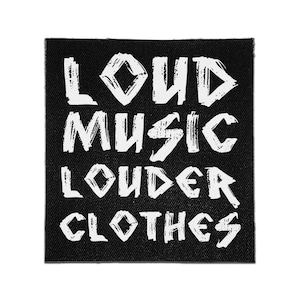 May include: A square black fabric patch featuring the white distressed-style text LOUD MUSIC LOUDER CLOTHES arranged in four horizontal lines. The lettering has a rough, textured appearance against the solid black background of the patch.