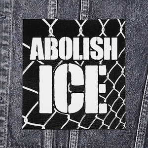 May include: A square black and white patch featuring the words "ABOLISH ICE" in bold, stencil-style lettering. The text is set against a chain-link fence graphic. The patch is likely made of fabric and is designed to be sewn or ironed on.