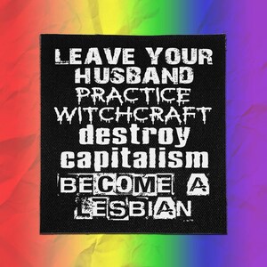 May include: A square black fabric patch featuring white text that reads: LEAVE YOUR HUSBAND, PRACTICE WITCHCRAFT, DESTROY CAPITALISM, BECOME A LESBIAN. The lettering uses a mix of distressed, gothic, and block fonts against a solid black background.