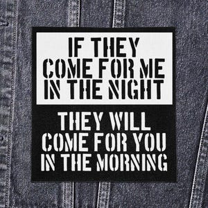 May include: A rectangular patch in black and white, featuring the text "IF THEY COME FOR ME IN THE NIGHT THEY WILL COME FOR YOU IN THE MORNING" in a stencil font. The patch is on a denim jacket.
