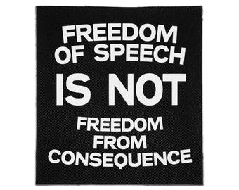 May include: A square black fabric patch featuring bold white text that reads: FREEDOM OF SPEECH IS NOT FREEDOM FROM CONSEQUENCE. The lettering is arranged in five lines with a clean, sans-serif font style against the dark, textured background.