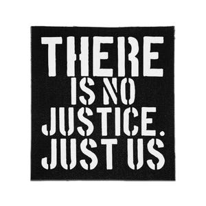 May include: A square black fabric patch featuring the white stencil-style text THERE IS NO JUSTICE. JUST US. The lettering has a distressed, industrial appearance with breaks in the characters, set against a solid black background with a visible weave.