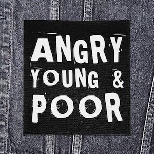 Peut inclure: Un écusson carré noir avec l'inscription blanche et audacieuse « ANGRY YOUNG & POOR ». L'écusson est présenté sur un fond en denim foncé, suggérant qu'il est destiné à être cousu sur des vêtements ou des accessoires.