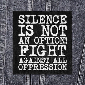 Peut inclure: Un écusson carré noir avec du texte blanc qui dit "SILENCE IS NOT AN OPTION! FIGHT AGAINST ALL OPPRESSION." L'écusson est affiché sur une veste en jean.