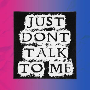 Könnte beinhalten: Ein quadratischer schwarzer Stoffaufnäher mit dem weißen Text JUST DONT TALK TO ME in einer abgenutzten Schablonenschrift. Die Buchstaben sind in vier Zeilen angeordnet, wobei jede Textzeile auf einem rauen, weiß gesprenkelten Hintergrund liegt.