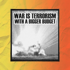 May include: A square fabric patch featuring a black and white halftone graphic of an explosion. The text WAR IS TERRORISM WITH A BIGGER BUDGET is printed in bold black capital letters on a white background at the top of the patch.