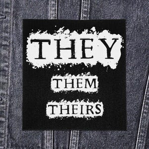 Op de afbeelding: Zwart vierkantige patch met de woorden "THEY", "THEM" en "THEIRS" in witte, schreefloze lettertypen. De woorden staan tegen een zwarte achtergrond, met een witte, gespatte rand. De patch wordt getoond op een spijkerjasje.